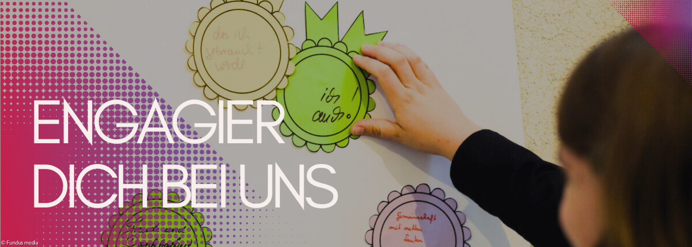 Schilder an einer Pinnwand. Darauf steht: gebraucht werden. Dankbarkeit und Zusammenhalt spüren. Davor steht eine Frau, die man von hinten sieht und gerade ebenfalls etwas an die Pinnwand hängt.