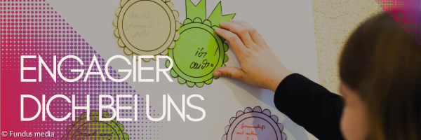 Schilder an einer Pinnwand. Darauf steht: gebraucht werden. Dankbarkeit und Zusammenhalt spüren. Davor steht eine Frau, die man von hinten sieht und gerade ebenfalls etwas an die Pinnwand hängt.