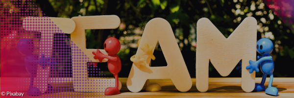 Holzbuchstaben TEAM vor Blätterhintergrund und kleine Figuren, die sich an den einzelnen Buchstaben festhalten.