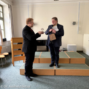 Pfr. Lehnen von der kathol. Nachbargemeinde Herz Jesu überreicht ein Geschenk